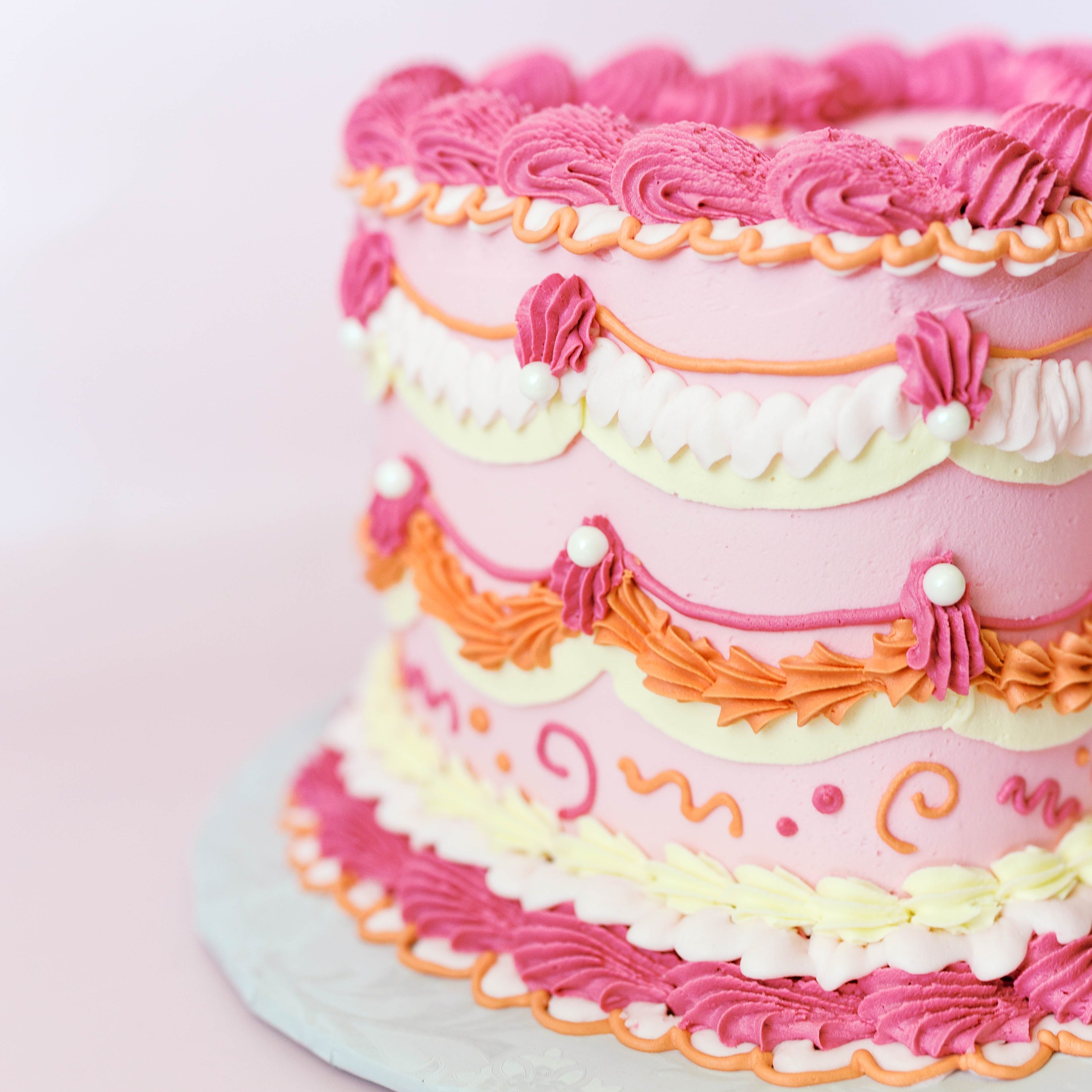 Multicolored cake with pink, orange, and yellow frosting on a light pink background