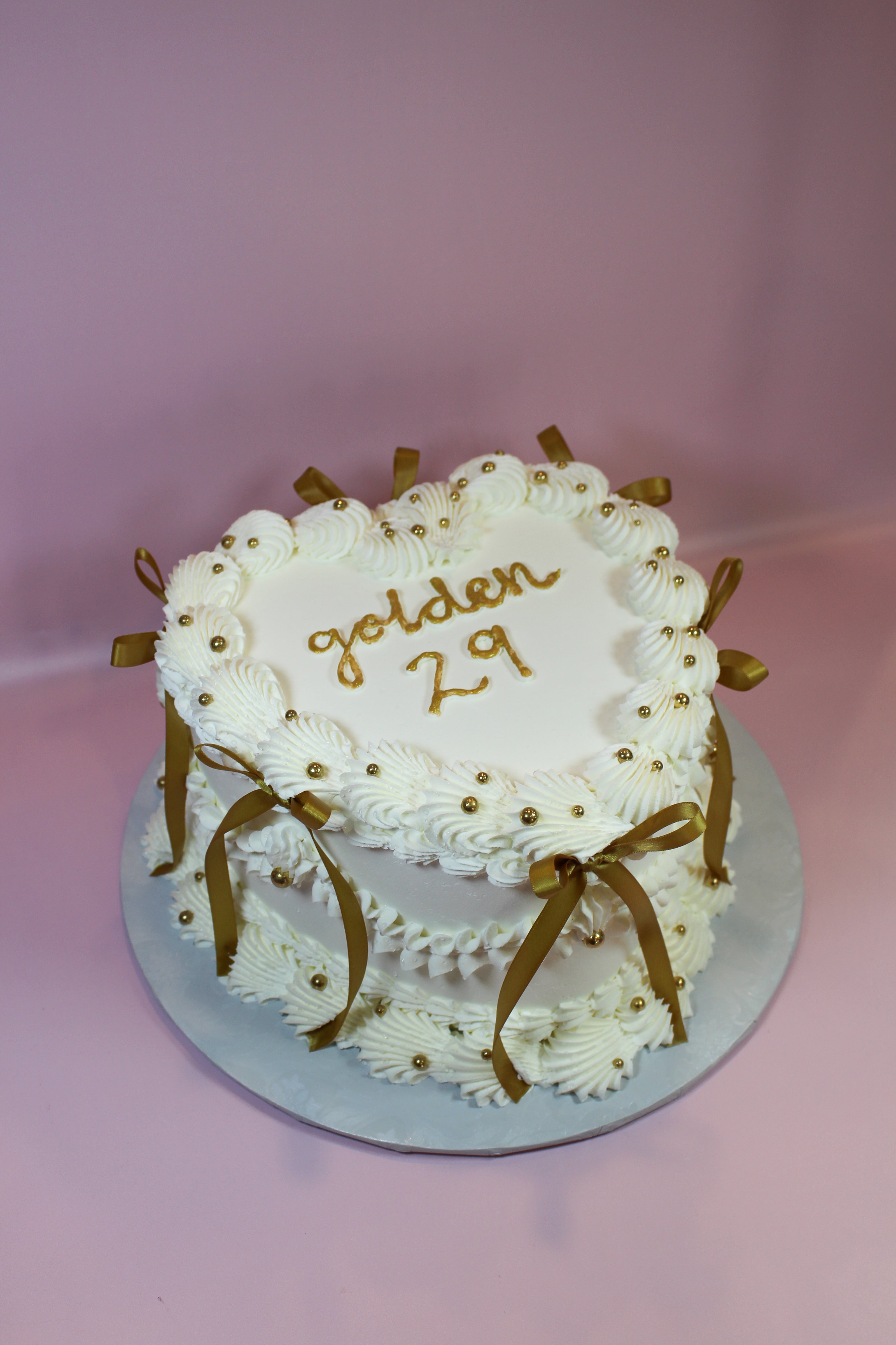 White cake with gold decorations and 'golden 29' text on a pink background