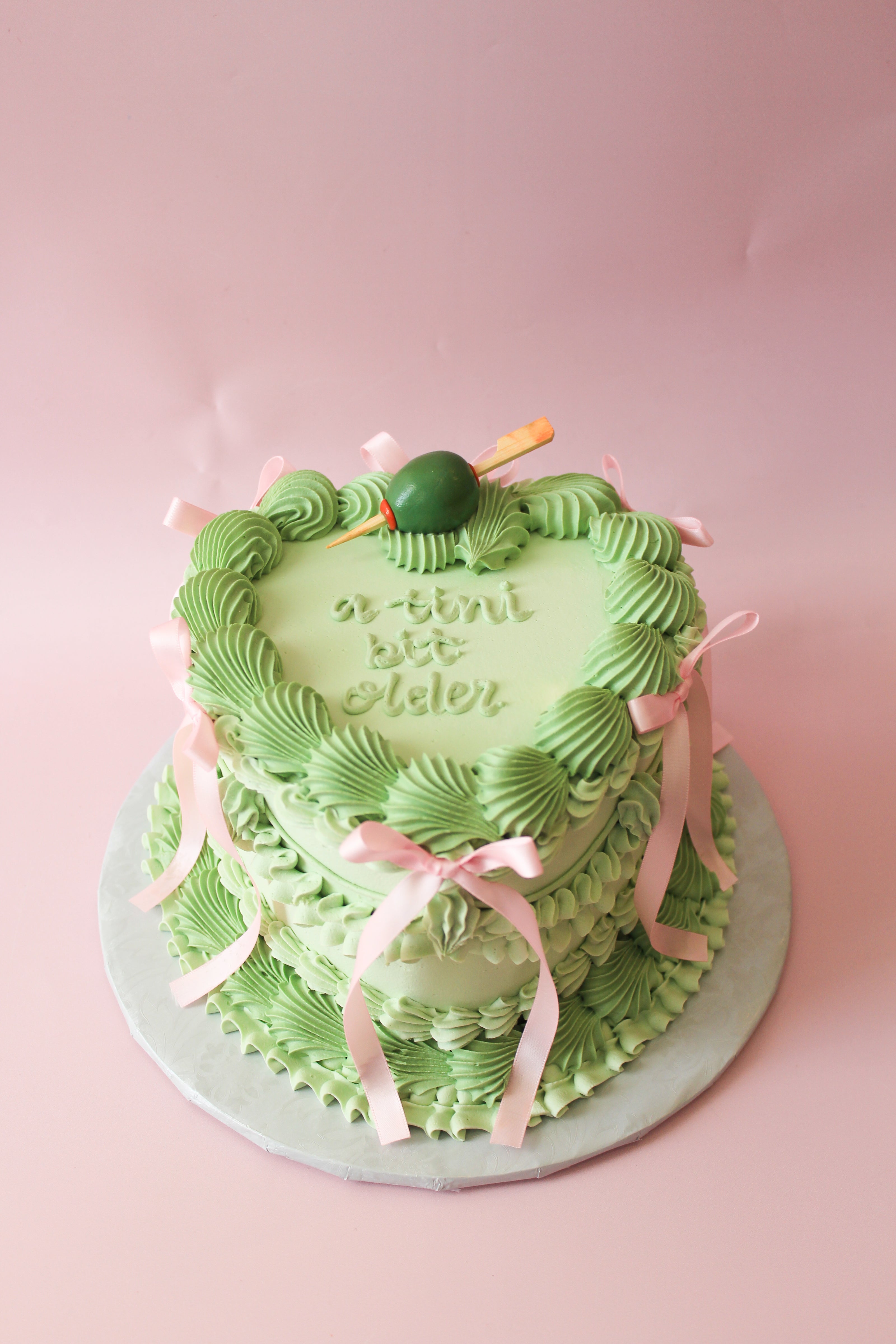 Green birthday cake with pink ribbons on a pink background