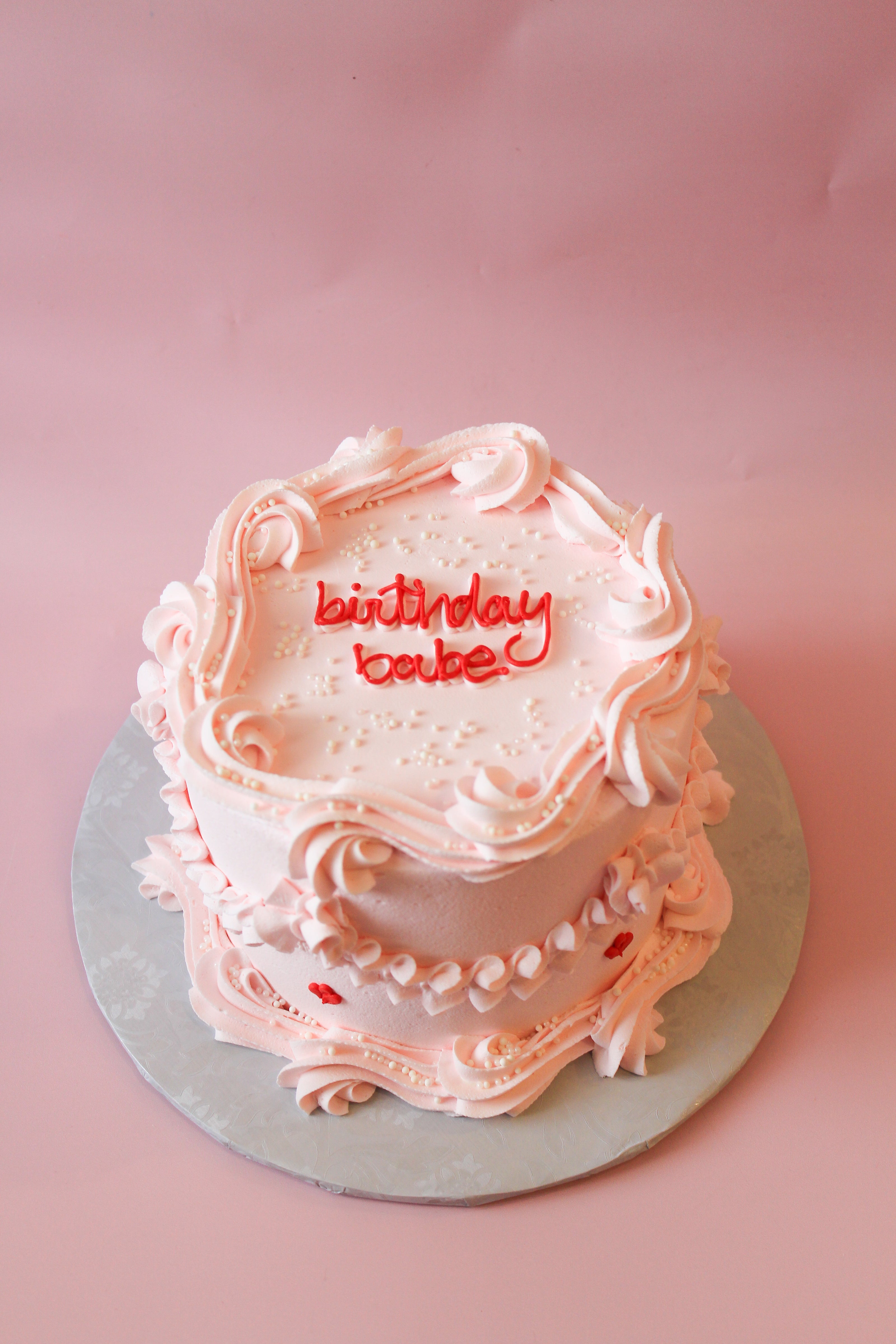 Two-tiered pink birthday cake with 'birthday cake' text on a pink background