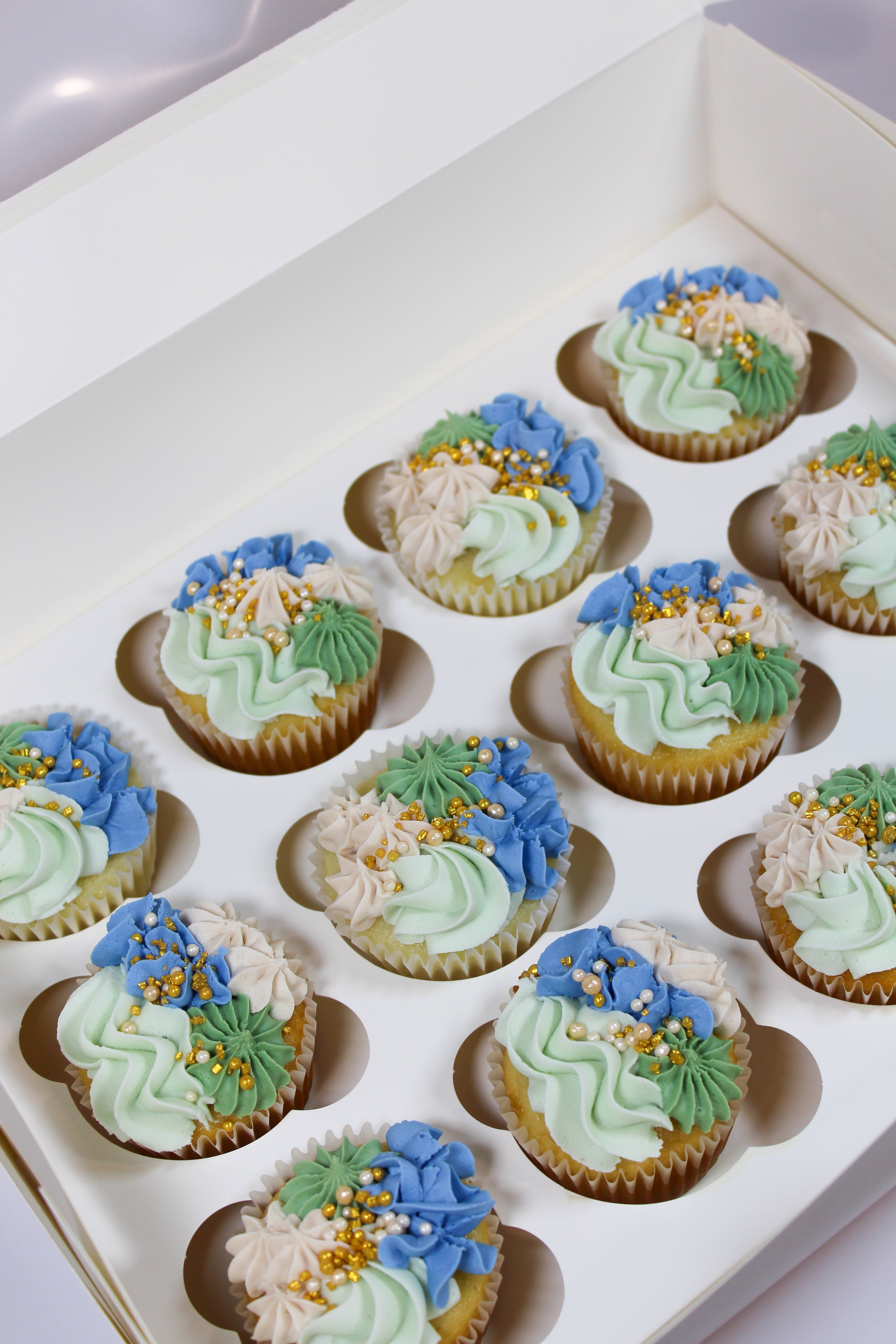 Decorative cupcakes with green and blue icing in a box