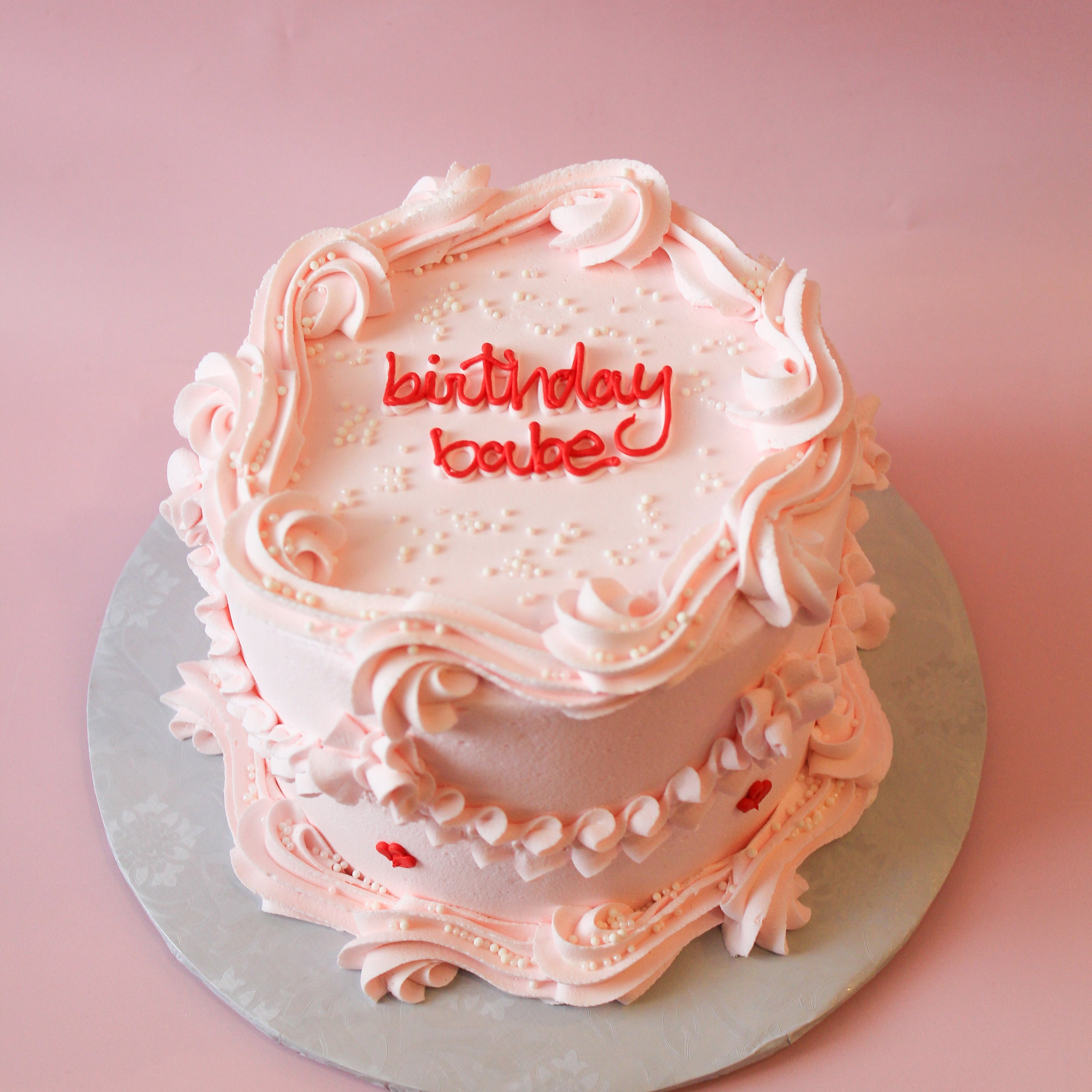 Two-tiered pink birthday cake with 'birthday babe' text on a pink background