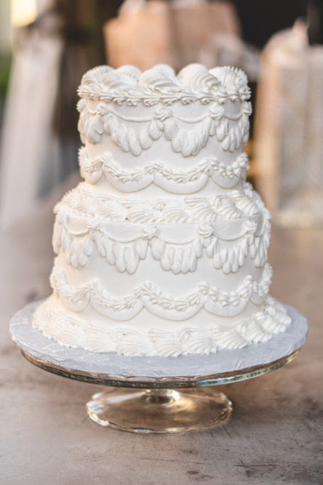 Three-tiered white wedding cake on a wooden table with blurred background