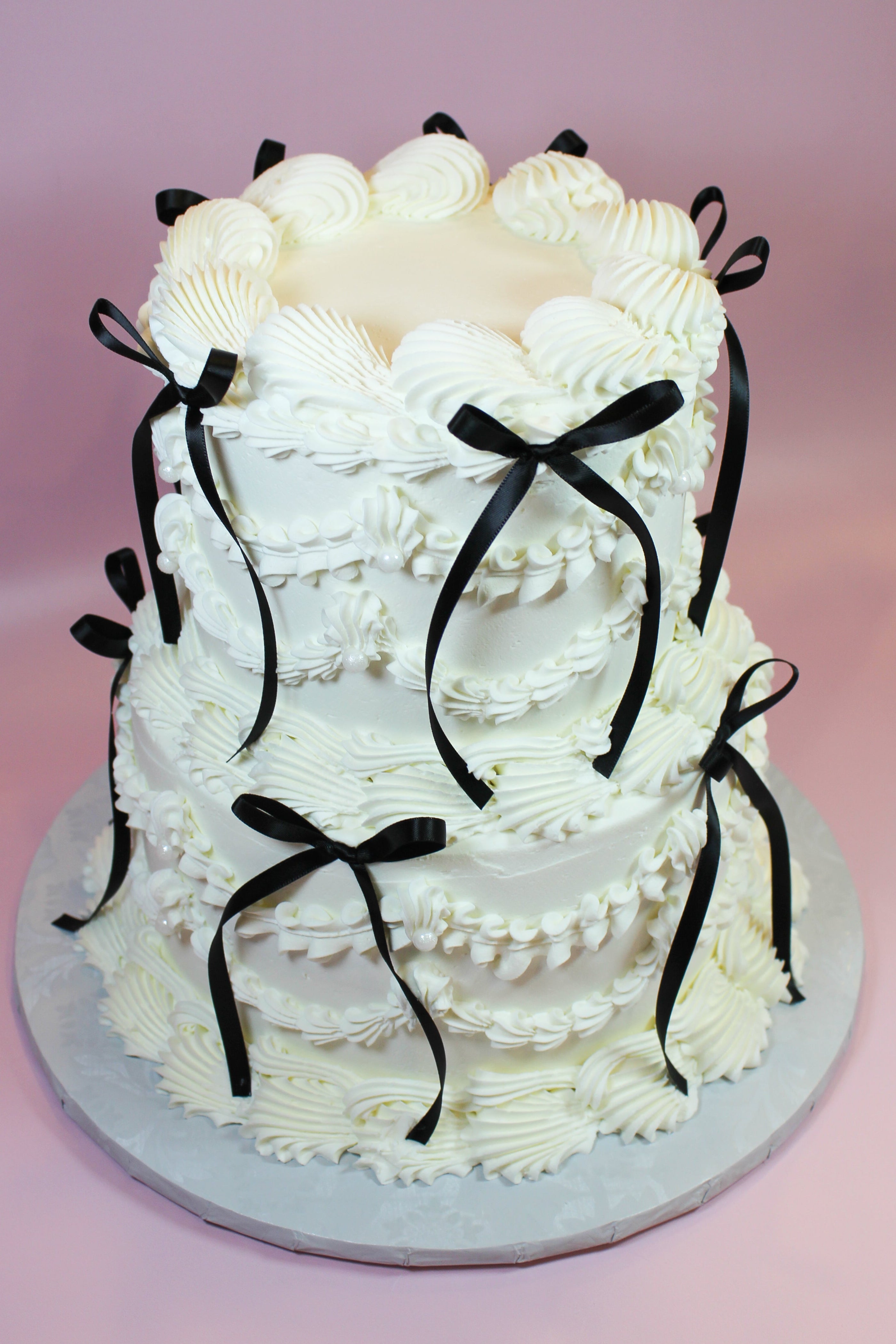 Two-tiered white cake with black ribbons on a pink background